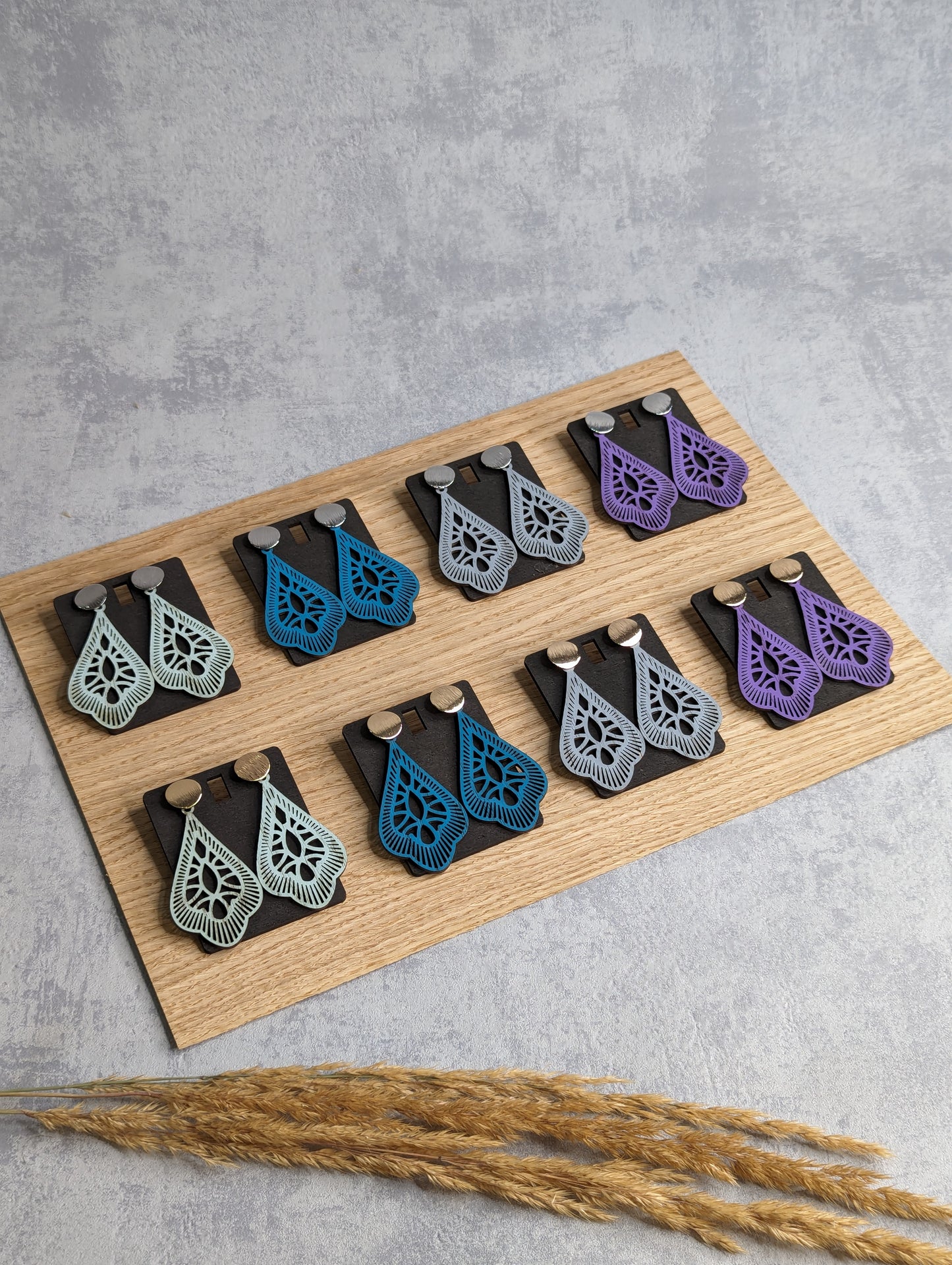 Handgefertigte Holzohrringe in Tropfenform mit filigranem Design, in verschiedenen Farben wie Blau, Grau, Lila und Mint.
