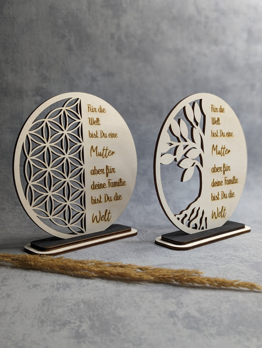 Zwei Holz-Dekoschilder mit der Gravur 'Für die Welt bist du eine Mutter, aber für deine Familie bist du die Welt'. Die Schilder zeigen geometrische und florale Muster und stehen auf dunklen Holzsockeln.