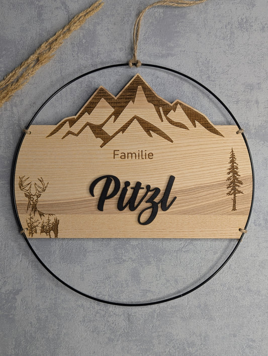 „Personalisiertes rundes Holz-Türschild mit Bergmotiv, Hirsch, Bäumen und Familienname Pitzl, graviert von Die Bildschneiderei