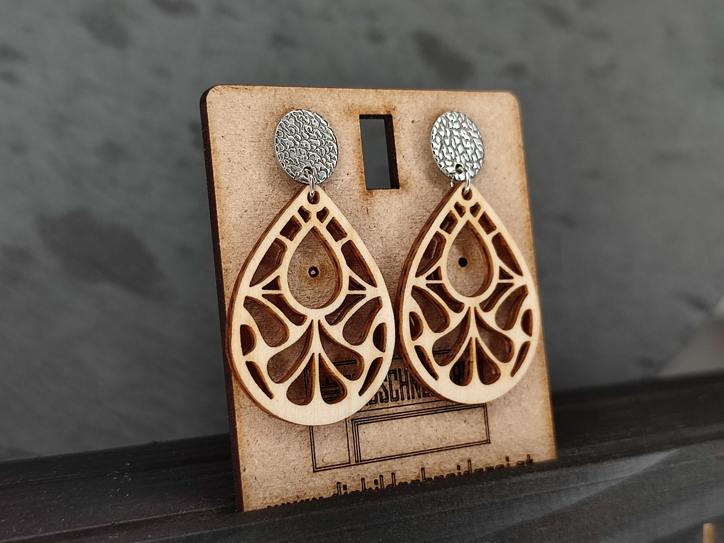 Handgefertigte Ohrringe aus Zirbenholz mit filigranem Tropfendesign und Edelstahl-Steckern mit strukturierter Oberfläche. Naturholz-Schmuck in leichter, eleganter Optik – ideal als stilvolles Accessoire oder Geschenk. Präsentiert auf einer Holzkarte mit Branding.
