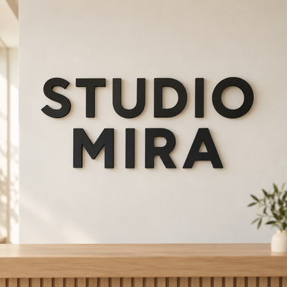 Schwarzer 3D-Firmenschriftzug STUDIO MIRA an einer hellen Wand über einer Empfangstheke