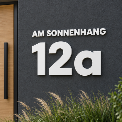 Weiße 3D-Hausnummer 12a mit kleinem Straßennamen AM SONNENHANG auf dunkler Fassade – Gestaltungsbeispiel aus zwei Konfigurationen