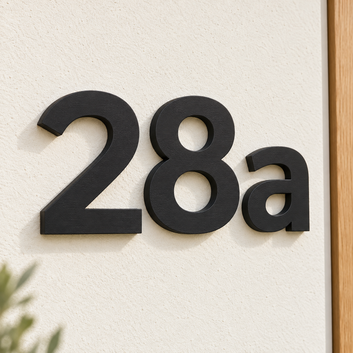 Schwarze personalisierte 3D-Hausnummer 28a an einer hellen Wand neben einer Holztür