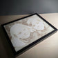 Personalisierte Lasergravur auf Holz mit einem Porträtmotiv von zwei Kindern. Das Bild ist in einem schlichten schwarzen Rahmen eingefasst und liegt auf einer Holzoberfläche. Die Gravur besticht durch feine Details und natürliche Holzstruktur.