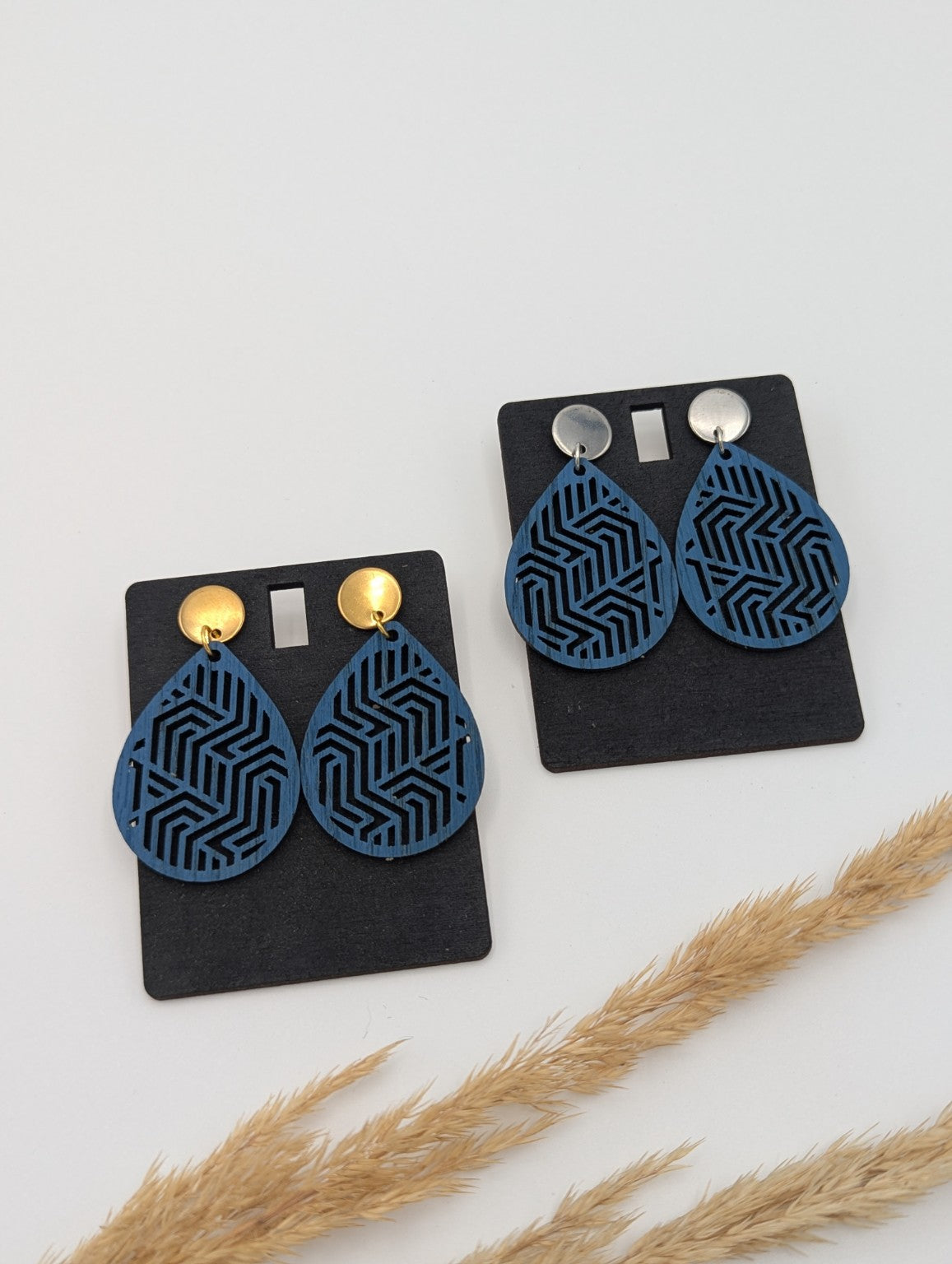 Zwei Paar blaue Tropfen-Holzohrringe mit geometrischem Linienmuster im Vergleich: links goldfarbene, rechts silberfarbene Stecker