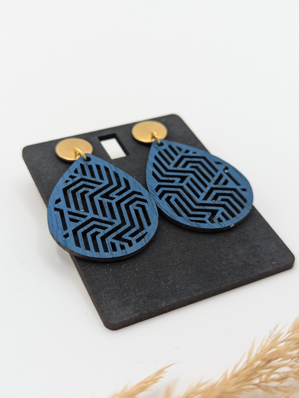Nahaufnahme der blauen Holzohrringe mit filigranem geometrischem Linienmuster und goldfarbenen Steckern