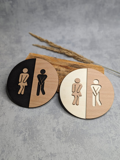 Rundes Toilettenschild aus Holz mit stilisierter Damen- und Herrenfigur, lasergraviert und in zwei Farbvarianten erhältlich.