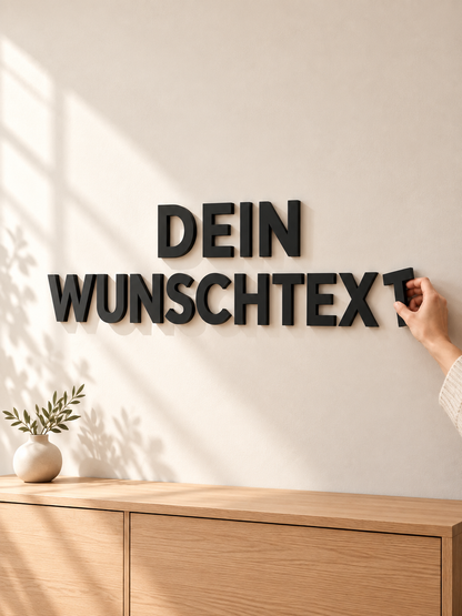 Schwarze 3D-Wandbuchstaben mit dem Schriftzug Dein Wunschtext an einer hellen Wand